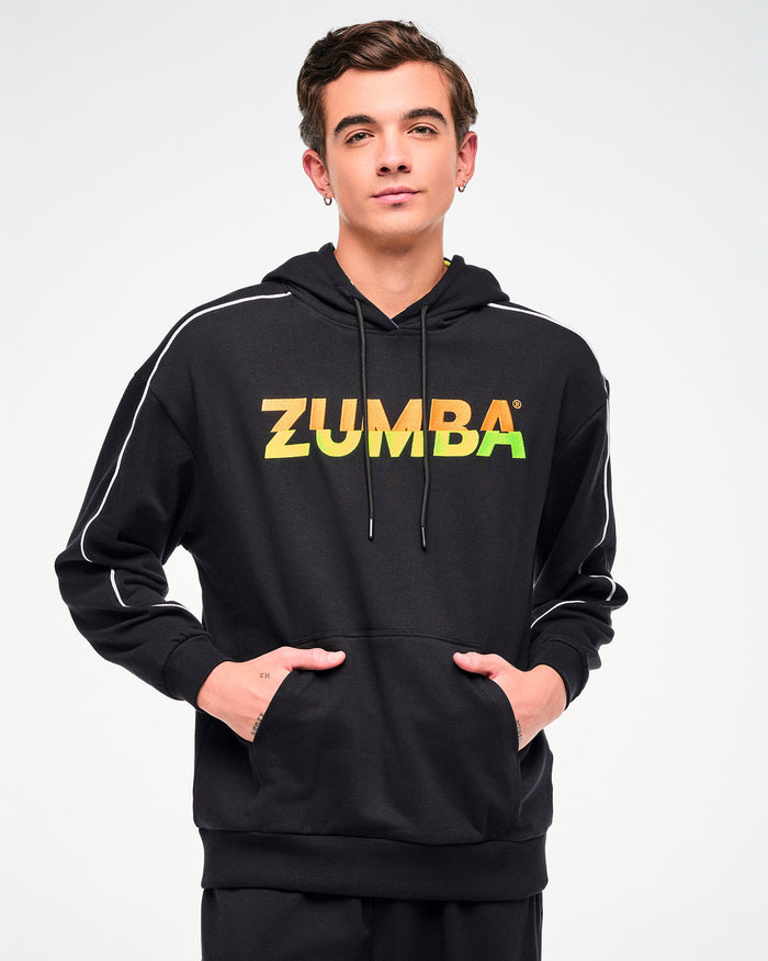 Close-up of a male model wearing a black hoodie with a gradient "ZUMBA" logo, shown with hands in the kangaroo hoodie pocket.