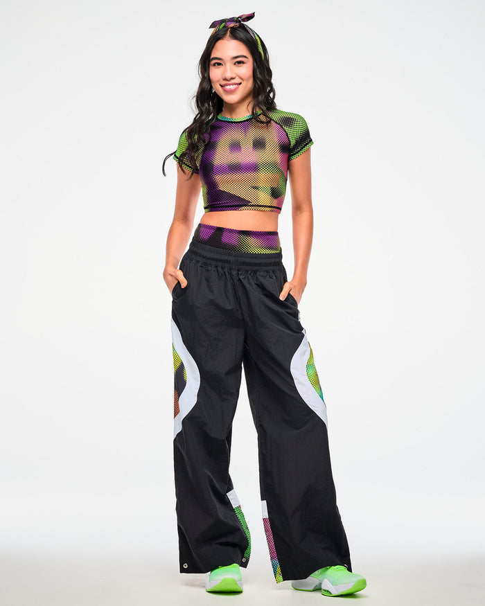 Female model wearing a dot-print crop top, paired with black track pants featuring a matching dot-print side panel and green sneakers.