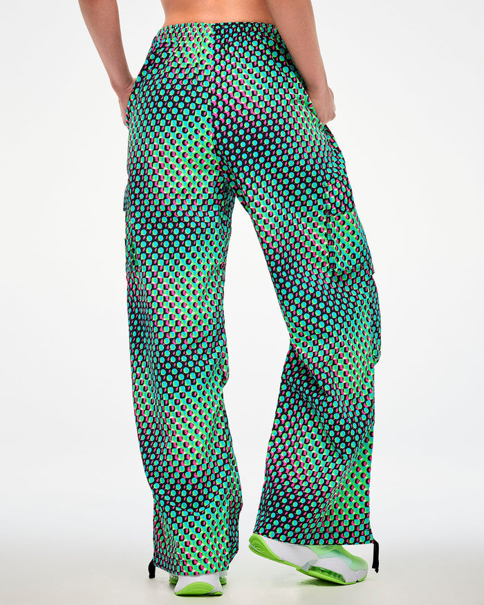 Shown from the back, female model wearing green cargo pants with an aqua, black, and pink dot print and green sneakers.