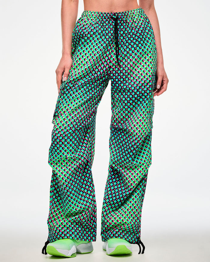 Female model wearing green cargo pants with black drawcords hanging over the aqua, black, and pink dot print, paired with green sneakers.