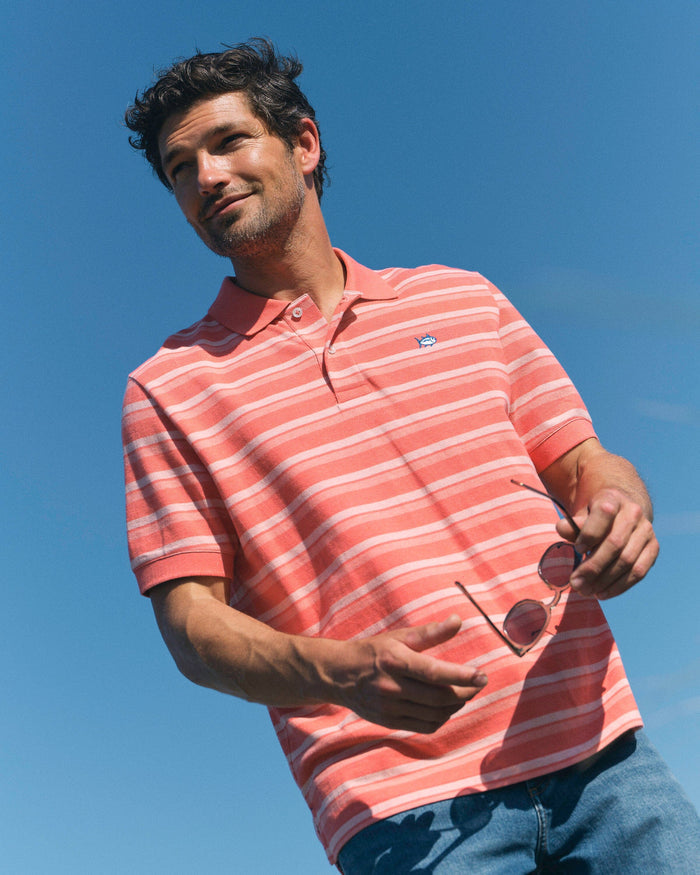 The lifestyle view of the Southern Tide Heather Striped Skipjack Polo by Southern Tide - Heather Coral Beach