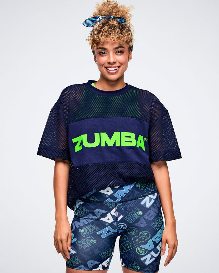 Female model in a Zumba outfit featuring a navy top, patterned shorts, and a blue bandana as a hair tie.