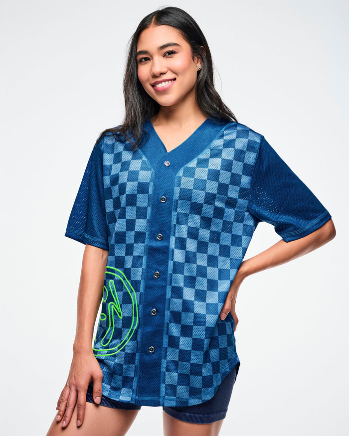 Female model wearing a blue checkered button up with a green Zumba logo on the lower right shown against a white background.