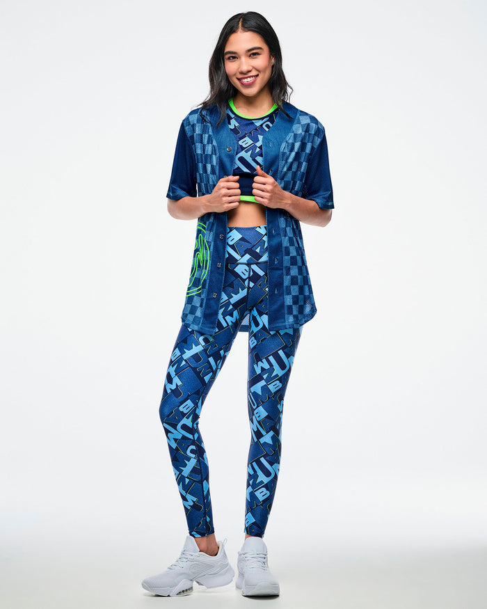 Female model wearing a blue checkered button-up jersey left open, with matching blue patterned bra and leggings, paired with white shoes.
