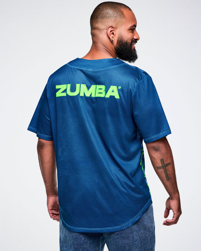 Male model, back view, wearing a blue button-up with “Zumba” in green across the upper back, paired with blue pants.
