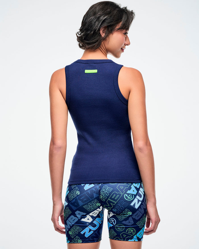 Back view of a female model showing the blue back of the tank, paired with blue Zumba print shorts.