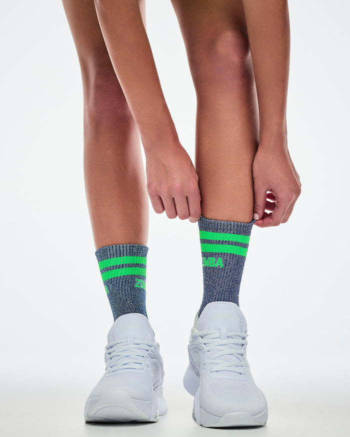Female model wearing indigo socks with green accents and white sneakers on a light gray background.