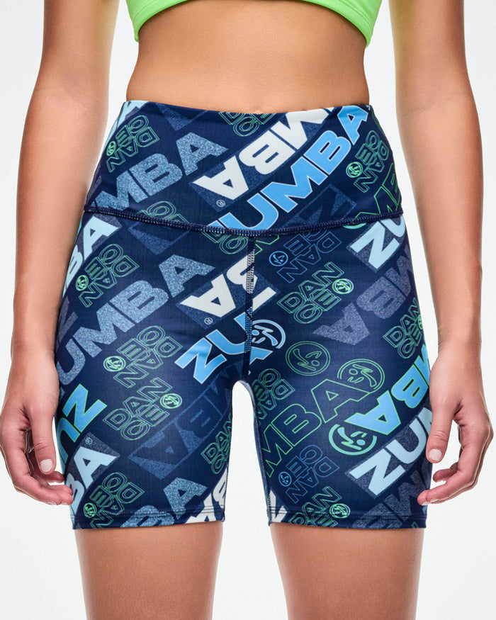 Close-up of a female model wearing navy biker shorts with a blue and green “ZUMBA” logo pattern.