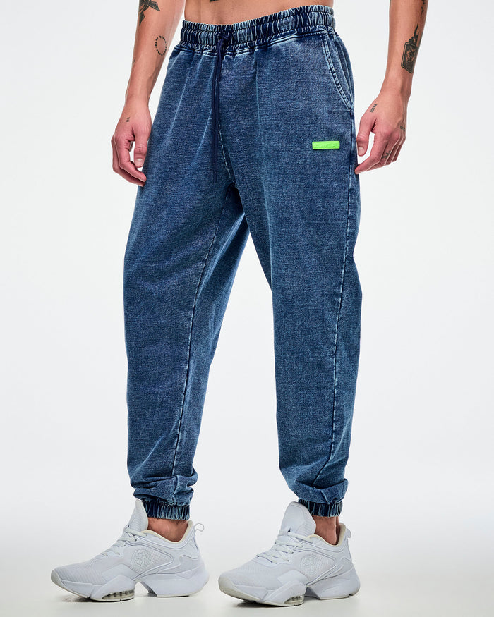 Male model wearing blue pants with a green "Zumba" label worn with white shoes on a white background.