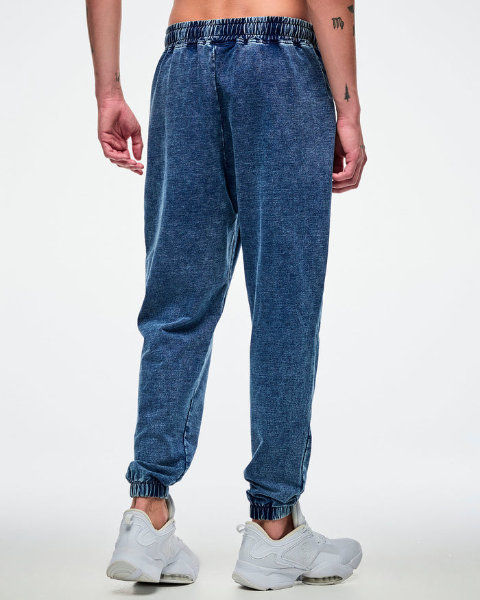 Back view of a male model wearing blue pants with white shoes on a white background.