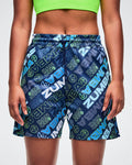Female model wearing blue patterned Zumba shorts with brand logo on a white background.