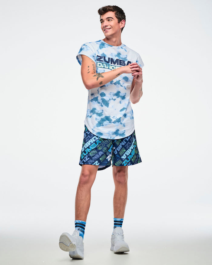 Full view of a male model in blue patterned shorts with both hands in his pockets, paired with a blue-and-white top and white shoes.