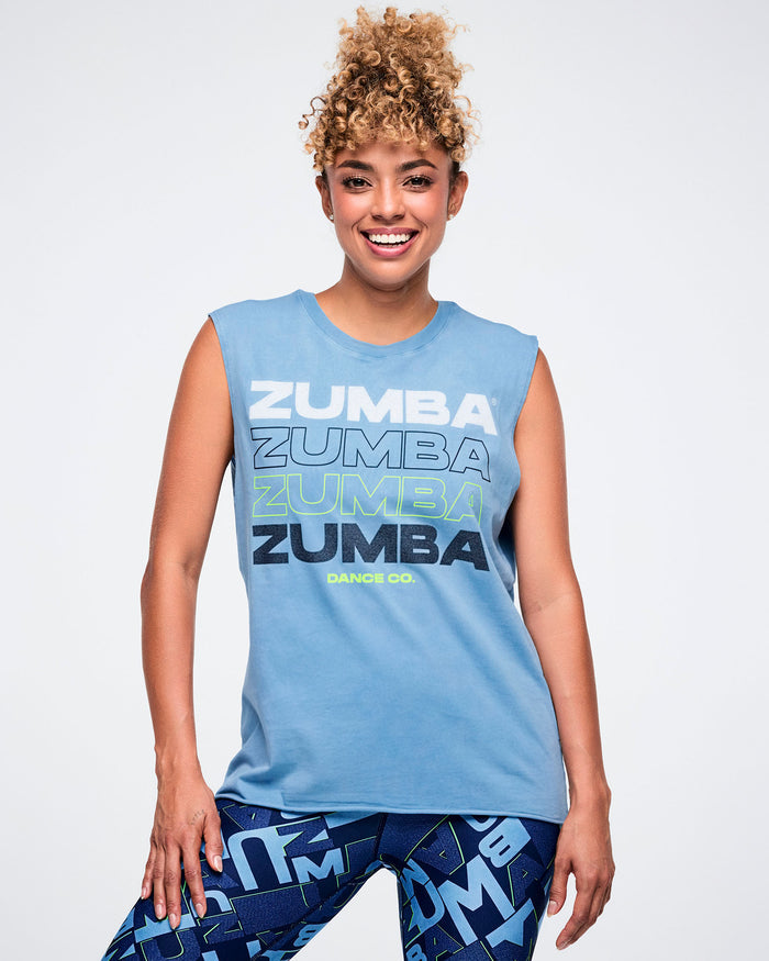 Female model wearing a light blue Zumba tank with “ZUMBA” in four text styles and “DANCE CO.” in smaller print.