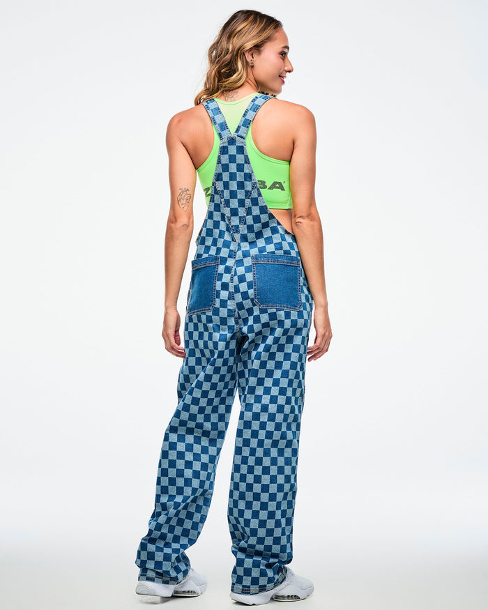 Back view of a female model wearing a neon green crop tank under checkered overalls, showing two standard blue denim back pockets, paired with white shoes.