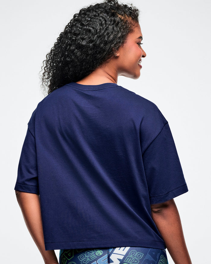 Back view of a female model wearing an indigo Zumba crop top on a white background.