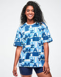 Female model wearing a blue patterned top with a plain background.