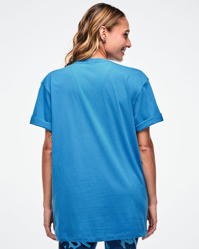 Back view of a female model wearing a light blue Zumba t-shirt on a white background.