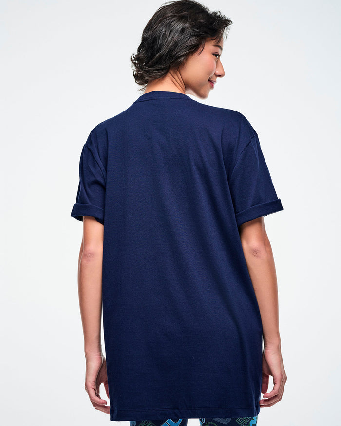 Back view of a female model wearing a dark blue Zumba t-shirt on a white background.