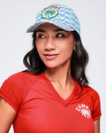 Light blue wavy-print baseball cap with a front “ZUMBA” palm-tree patch and curved brim, modeled by a female wearing a red V-neck tee on a white studio background.