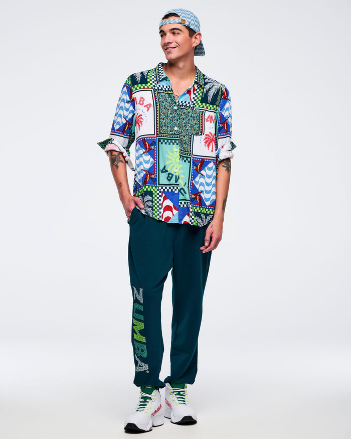 Light blue wavy-print baseball cap worn backward, showing the adjustable strap and metal buckle, styled on a male wearing a multicolor printed button-up shirt, teal joggers, and white sneakers on a white studio background.
