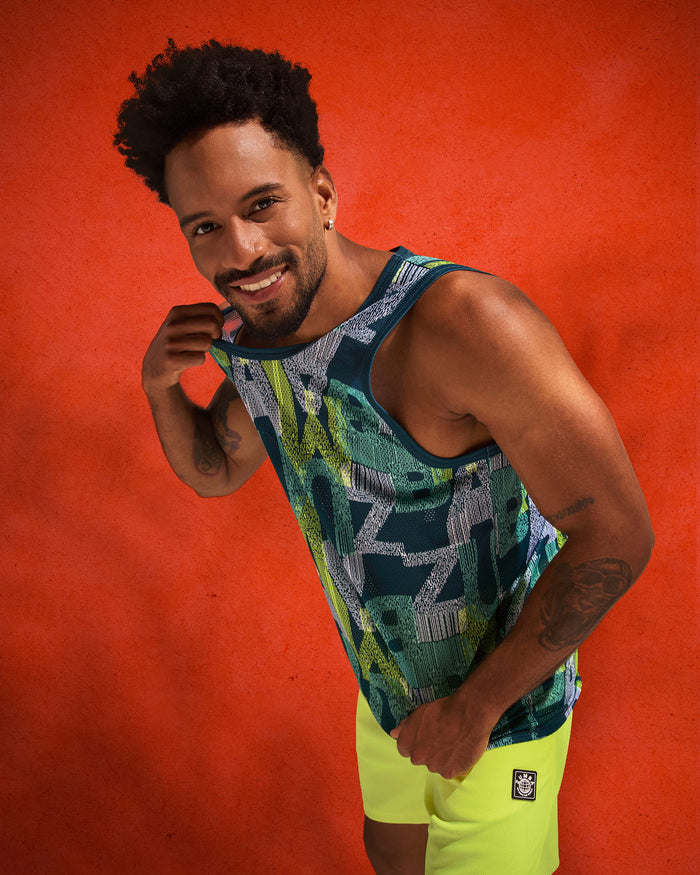 Teal, navy, and lime graphic-print mesh tank top paired with neon lime shorts, modeled by a male leaning forward against a textured orange backdrop.