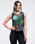 Tropical-print sleeveless mesh tank with black trim and multicolor leaf, palm, and parrot graphics; female model wears high-waisted black leggings, posing on a white background.
