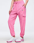 Front view of pink Zumba cargo joggers with elastic waistband and drawcord, side pockets, and a flap cargo pocket, worn by a female model with white-and-pink sneakers.