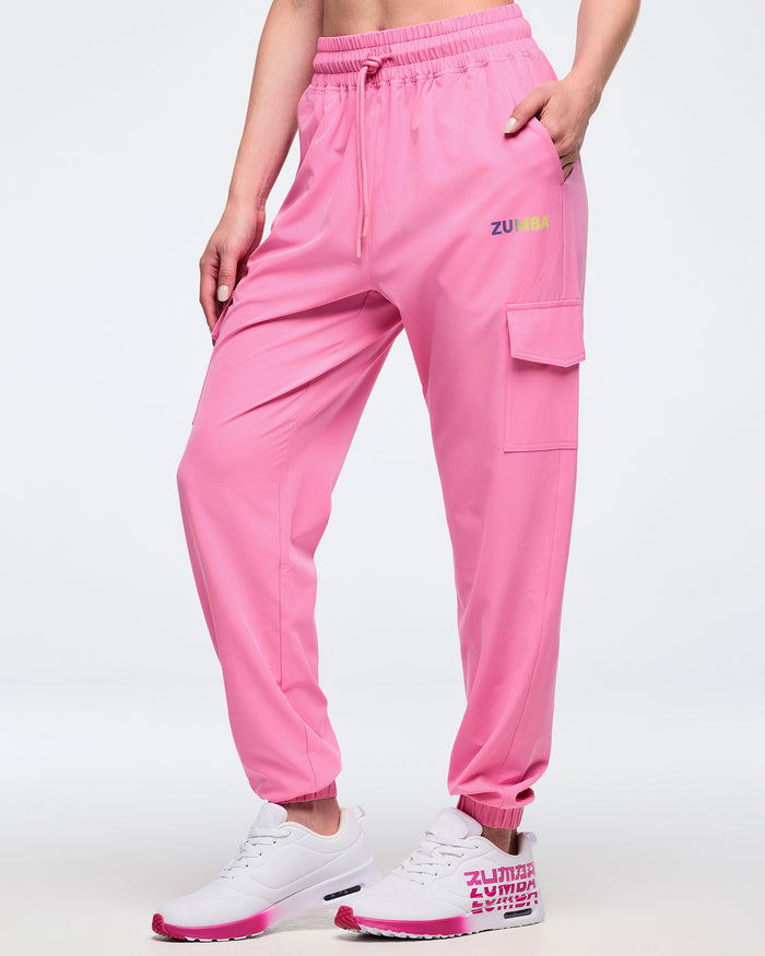 Front view of pink Zumba cargo joggers with elastic waistband and drawcord, side pockets, and a flap cargo pocket, worn by a female model with white-and-pink sneakers.