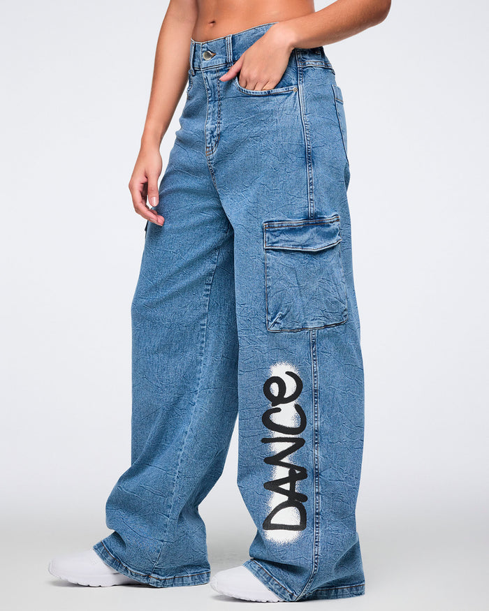 Female model wearing blue cargo pants with 'DANCE' spray painted on the pant against a white background.