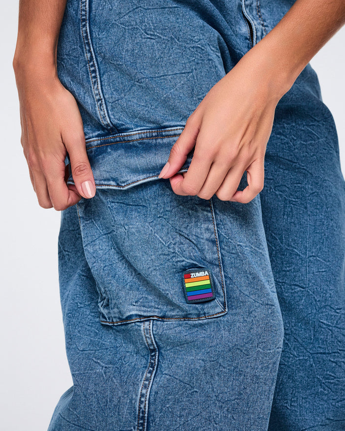 Female model close‑up showing denim cargo pocket with rainbow Zumba patch against a white background.