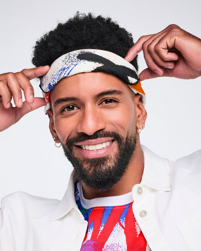 Close up of a male model adjusting a colorful bandana against a white background.