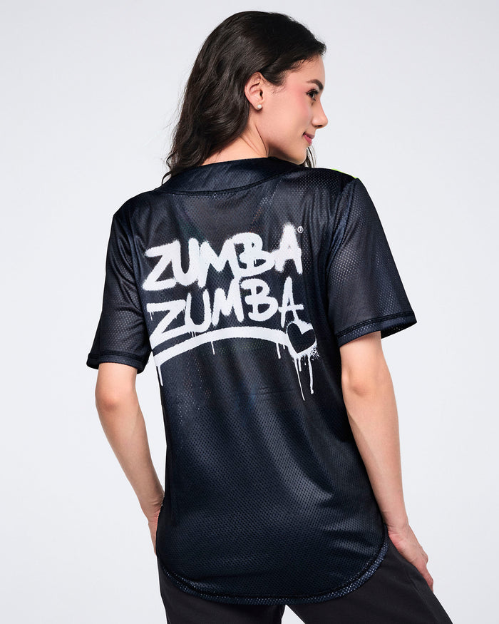 Female model showing the back of a black mesh Zumba jersey with white “Zumba Zumba” graffiti text with a heart on a white background.