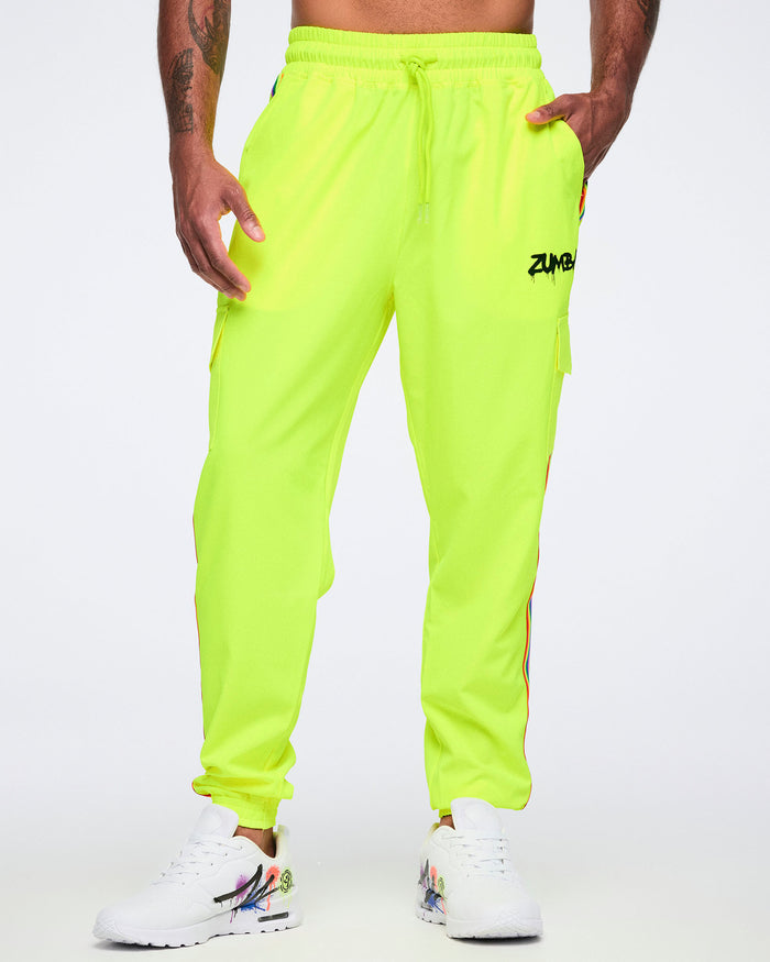 A male model wearing bright yellow pants featuring a graffiti-style “Zumba” logo on the upper left leg, with his hand in the left pocket, all paired with white graffiti-style sneakers, against a white background.