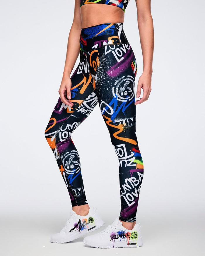 Female model wearing vibrant, graffiti‑inspired leggings featuring multicolored artwork on a black base, set against a white background.