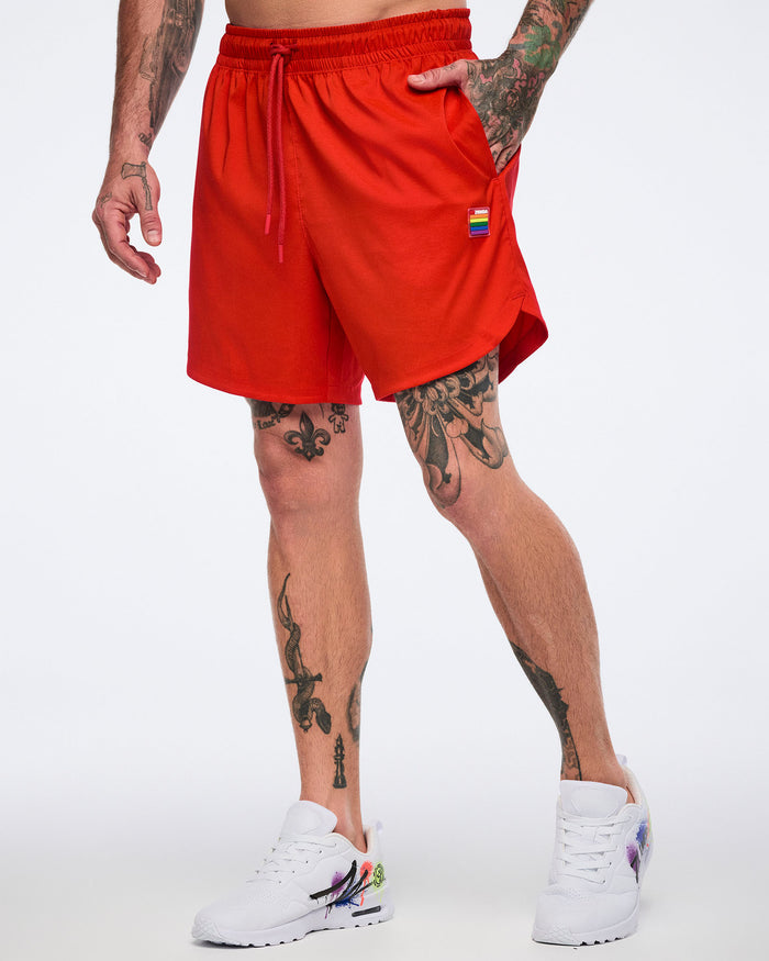 Male model wearing red shorts with a brand logo wearing white 'Zumba' shoes on a white background.