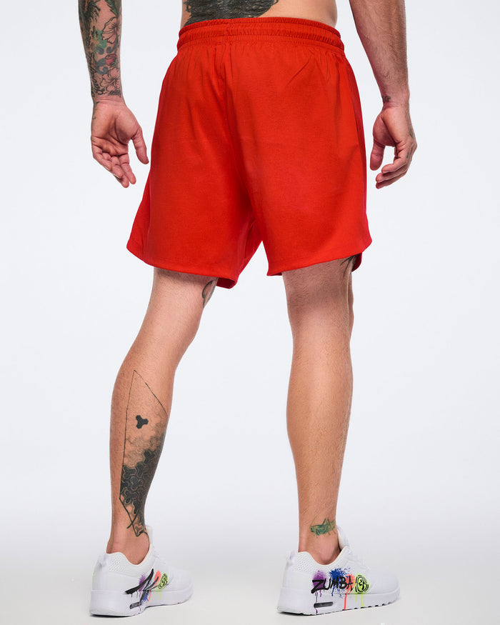 Male model, shown from the back, wearing red shorts and white 'Zumba' sneakers with colorful designs on a white background.