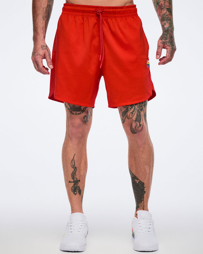 Male model wearing red shorts with a drawstring and white 'Zumba' sneakers on a white background.