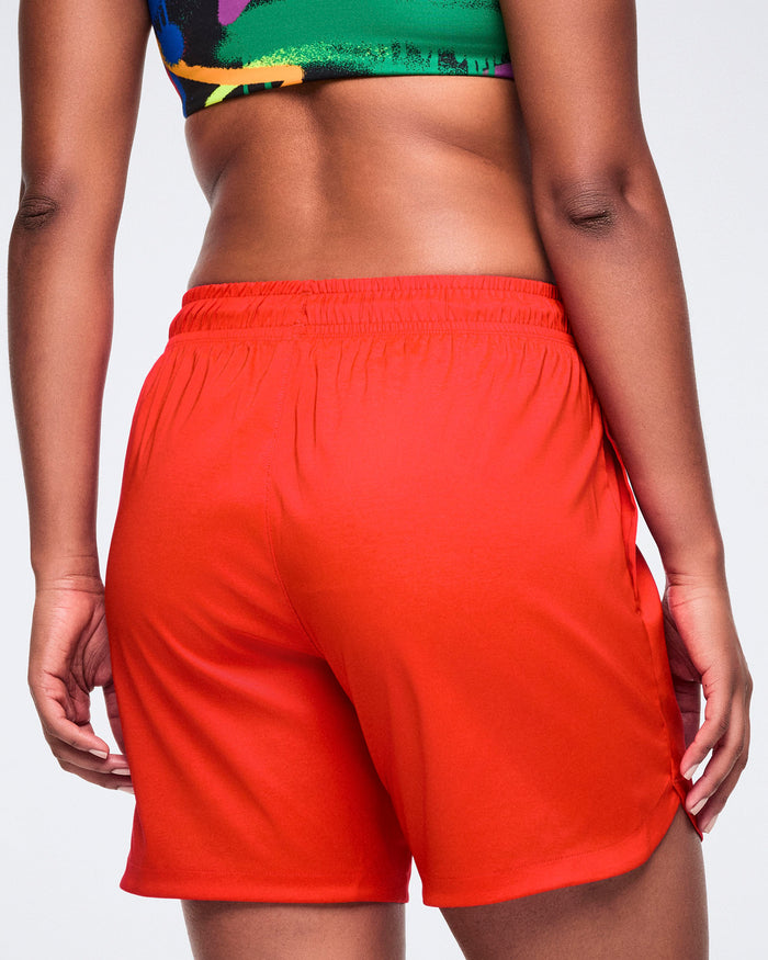 Back view of a female model wearing red shorts and a colorful bra on a white background.