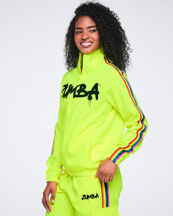 Female model from the side wearing a bright yellow Zumba jacket and matching pants with rainbow stripes on a white background.