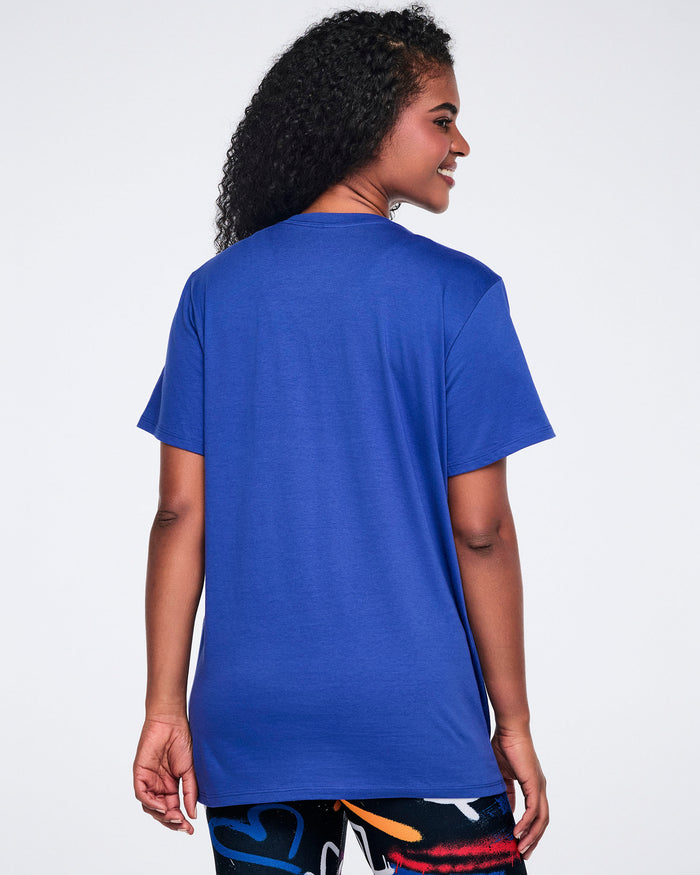 Back view of a female model wearing a blue t-shirt and colorful leggings on a white background.