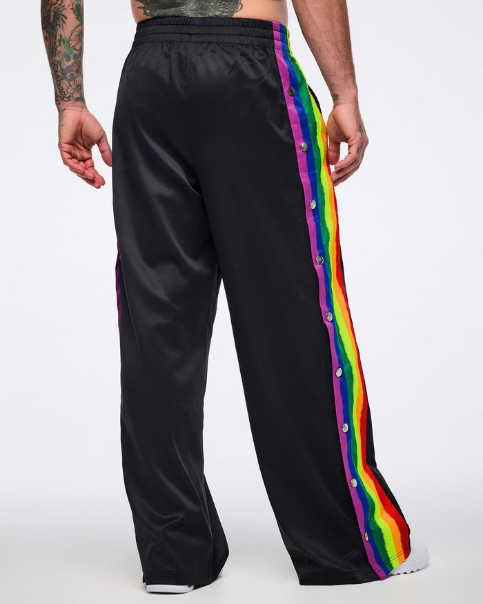 Male model shown from the back in black track pants with rainbow side stripes and white sneakers against a white background.