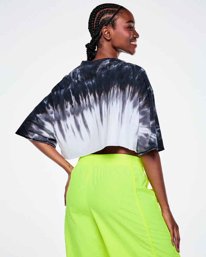 Back view of a female model wearing a cropped tie-dye Zumba top, paired with yellow pants.