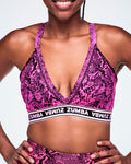 A close-up of a female model wearing a pink and black snakeskin-patterned sports bra with a white and black under band printed with 'ZUMBA' in white letters.