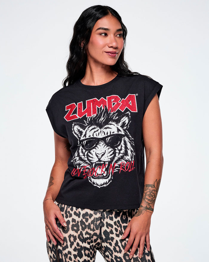 A female model wearing a black tank with a large graphic print of a black and white tiger wearing sunglasses and the word 'ZUMBA' in red rock-like text on the top and "LOVE + ROCK N' ROLL", over the tigers mouth, all paired with leopard print leggings.