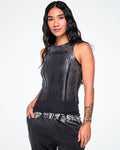 A female model wearing a sleeveless black Zumba ribbed tank top with a subtle metallic sheen and 'ZUMBA' printed across the chest, in smaller black text, paired with dark pants, against a plain white studio background.