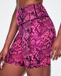 A close-up of a female model wearing high-waisted biker shorts with a vibrant pink and black snakeskin pattern.