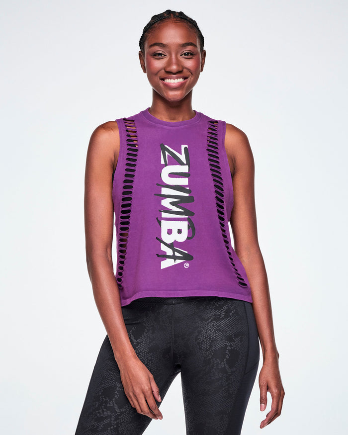 A female model wearing a purple sleeveless loose muscle tank with cut slashes along sides of front body, with 'ZUMBA' text vertically in white and black, paired with black leggings.