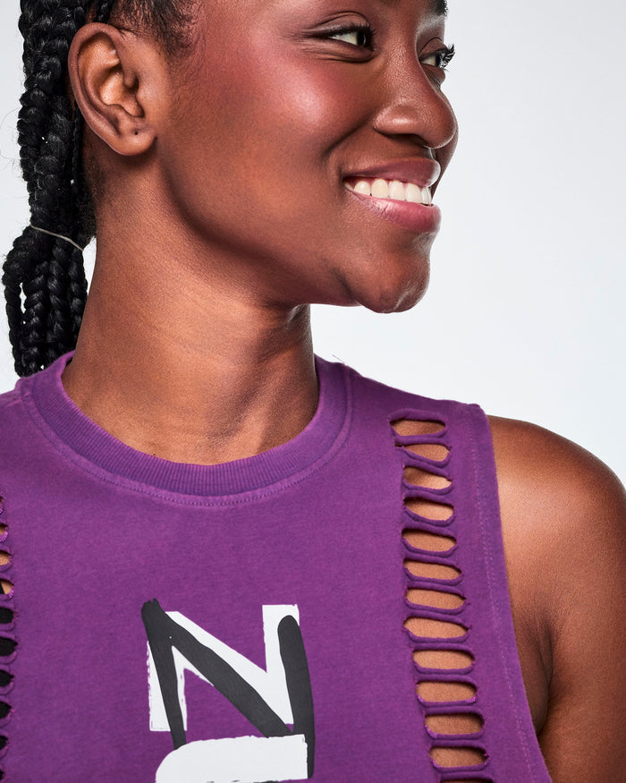 A female model wearing a purple sleeveless loose muscle tank with a close-up of the cut slashes along sides of front body.