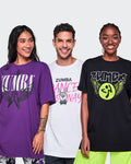 Three models wearing Zumba graphic t-shirts in purple, white, and black, standing against a white studio background.