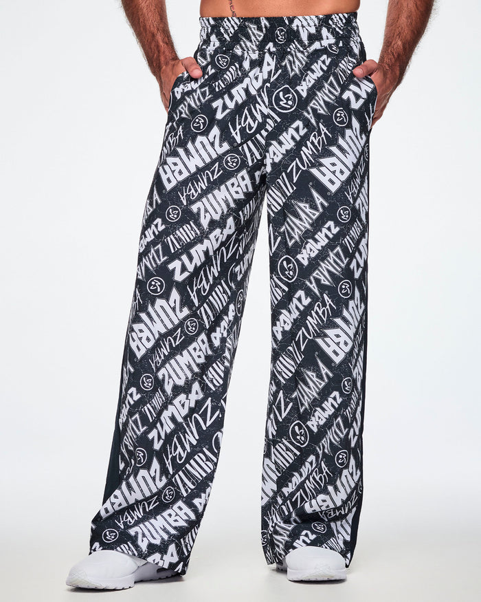 Front view of a male model wearing black and white Zumba rock branded track pants and paired with white shoes.
